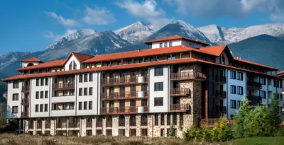 a large building with mountains in the background at Grand Royale Apartment Complex & Spa in Bansko