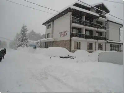 a building covered in snow with snow covered cars at Family hotel Iskar in Govedartsi
