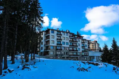 a large apartment building in the snow with trees at Aparthotel Pine Hills Pamporovo in Pamporovo