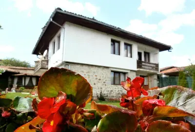 a house with red flowers in front of a house at The Gates Apartments in Koprivshtitsa