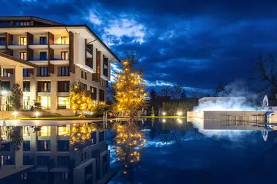 a hotel with a reflection in the water at night at Kamengrad Hotel & SPA in Panagyurishte