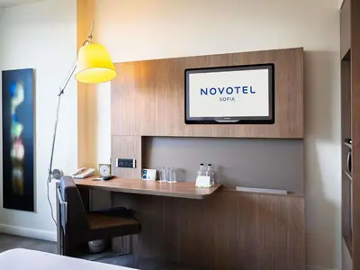 a hotel room with a desk with a tv on a wall at Novotel Sofia in Sofia
