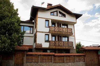 a white house with wooden balconies and a fence at Guest House Ilinden in Bansko