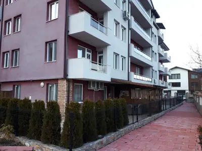 a pink building with a fence next to a brick sidewalk at ApartVel apartment 3 in Velingrad