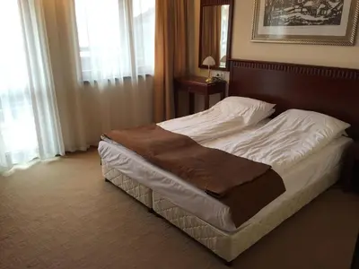 a bed in a hotel room with white sheets and brown blanket at Downtown Alexander Services Apartments in Bansko