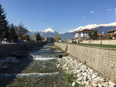 a river with a stone wall and mountains in the background at Cedar Lodge 3/4 Apartment Paradise in Bansko