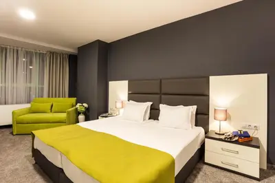 a bedroom with a large bed and a green chair at Earth & People Hotel & SPA - Free Parking & Swimming Pool in Sofia