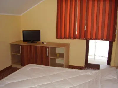 a bedroom with a bed with red curtains and a television at Guest House Goranovi in Velingrad