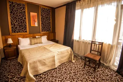 a bedroom with a bed and a chair and windows at Elida Family Hotel in Bansko