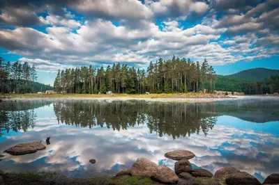a lake with trees and clouds in the sky at Romantica Forest Guest House in Dospat