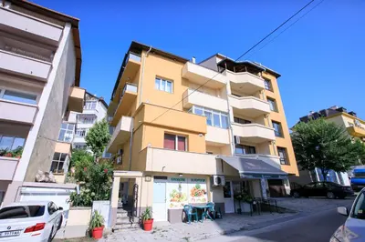 a tall yellow building with cars parked in front of it at Апартамент Рози in Sandanski