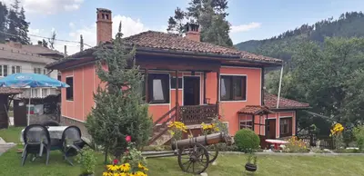 a small orange house with a wheelbarrow in a yard at Mechta Guest House in Koprivshtitsa