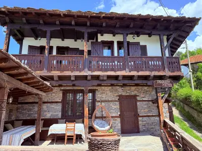 a wooden house with a balcony with a table and chairs at Къща за гости Родопски изгрев in Leshten
