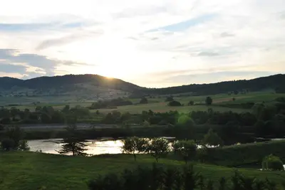 a sunset over a green field with a river at Хотел Планински кът in Dorkovo