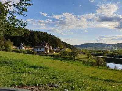 a green field with houses on a hill next to a river at Хотел Планински кът in Dorkovo