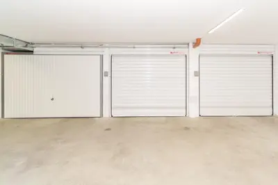 three white garage doors in a room with a concrete floor at Plovdiv City Center Kapana with garage in Plovdiv