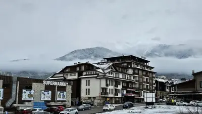 a building in a town with snow covered mountains at NEXT TO GONDOLA. Cosy & Elegant 2 Bedroom apartment in Neon Complex in Bansko