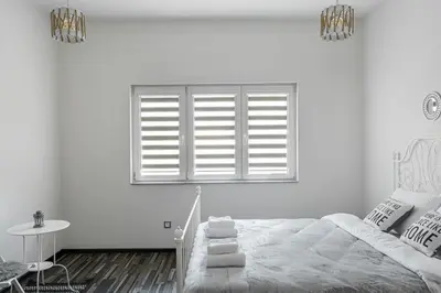 a white bedroom with a bed and a window at Gladstone suites in Plovdiv