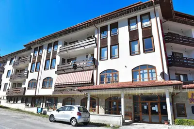 a white building with a car parked in front of it at Cedar Lodge in Bansko