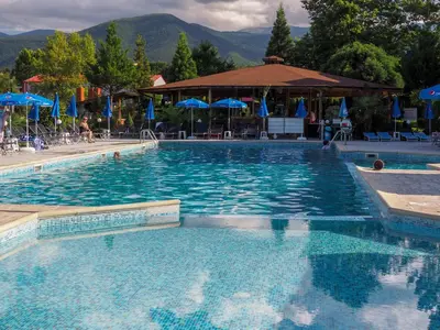 a large swimming pool with chairs and blue umbrellas at Dolna Bania Hotel in Dolna Banya