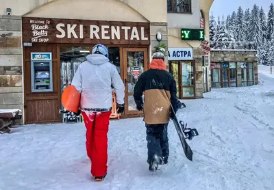 two people walking in the snow with a snowboard at Апартамент Pamporovo Palace in Pamporovo