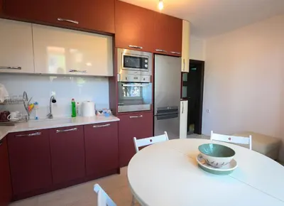 a kitchen with red cabinets and a white table at Апартамент за гости Римски терми in Kyustendil