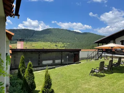 a yard with chairs and a building with mountains in the background at ПАУНОВАТА КЪЩА in Yasă-Koriya