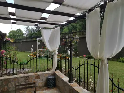 a pergola with white curtains on a fence at Мирков Дар in Bansko
