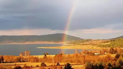a rainbow in the sky over a lake at Вили Green in Tsigov Chark