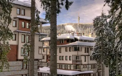 a hotel in the snow with trees in the foreground at Ски студио Снежанка в Грийн лайф Пампорово in Pamporovo
