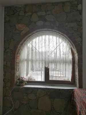 a window in a stone wall with a window with white curtains at Лилянината къща in Kalofer