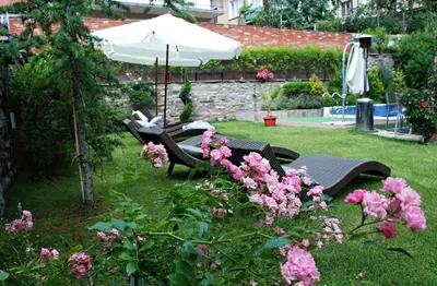 a garden with chairs and an umbrella and pink flowers at Villa Vuchev in Velingrad