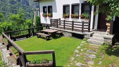 a yard with benches and a house with flowers at Авина къща in Kovachevitsa