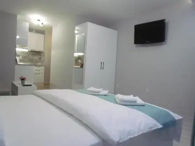 a white bedroom with a bed with a tv on the wall at Апартаменти Елеганс in Sandanski