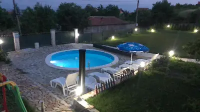 a pool with chairs and umbrellas in a yard at night at Sunshine villa Dzhigurovo in Sandanski