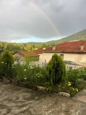 a rainbow over a garden with flowers and a house at Къща за гости 