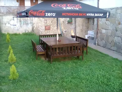 a wooden table and benches under a cocacola umbrella at Katya Guest House in Smolyan