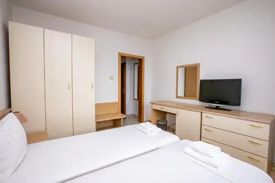 a bedroom with two beds and a desk with a television at Hotel Astra in Sandanski