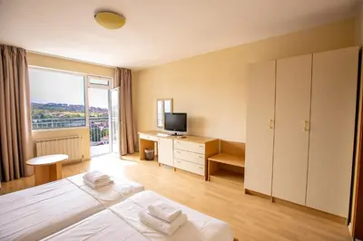 a bedroom with two beds and a desk with a television at Hotel Astra in Sandanski