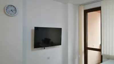 a flat screen tv hanging on a wall with a clock at Парк Апартаменти Юлия in Sandanski