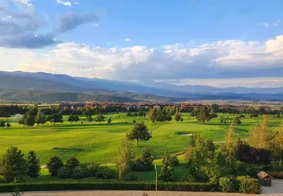 a green field with trees and houses in the distance at Mountain View Pirin Golf in Bansko