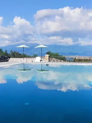 a pool of blue water with umbrellas in the background at Leshtenski Rai Guest House in Leshten