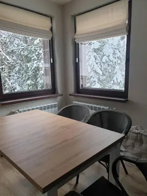 a dining room with a wooden table and two windows at All Seasons Apartments Borovets Gardens in Borovets