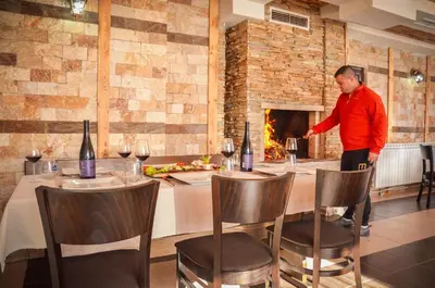 a man standing at a table in a restaurant with a fireplace at Family hotel Andreev in Dobrinishte