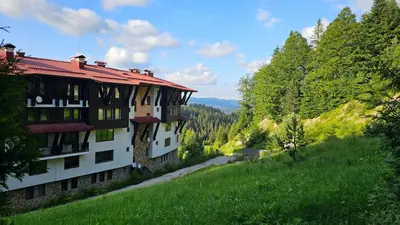 a building on the side of a hill with trees at Апартамент Amare, Гранд Манастира in Pamporovo