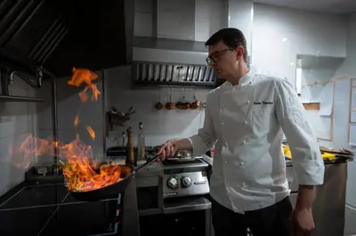 a man cooking food in a pan in a kitchen at VIZUALIZA Residence Hotel by HMG in Plovdiv