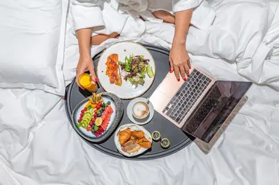 a person in bed with a tray of food and a laptop at VIZUALIZA Residence Hotel by HMG in Plovdiv