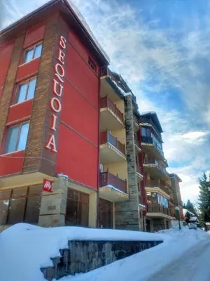 a hotel with a red building in the snow at Kolimechkov Apartments Borovets in Borovets