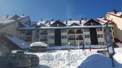 a snow covered building with cars parked in front of it at Deluxe Apartments in Pamporovo