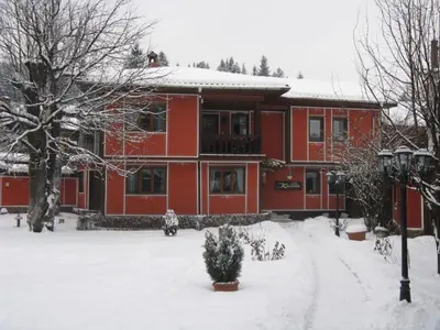 a red house with snow on the ground in front of it at Family Hotel Kalina in Koprivshtitsa